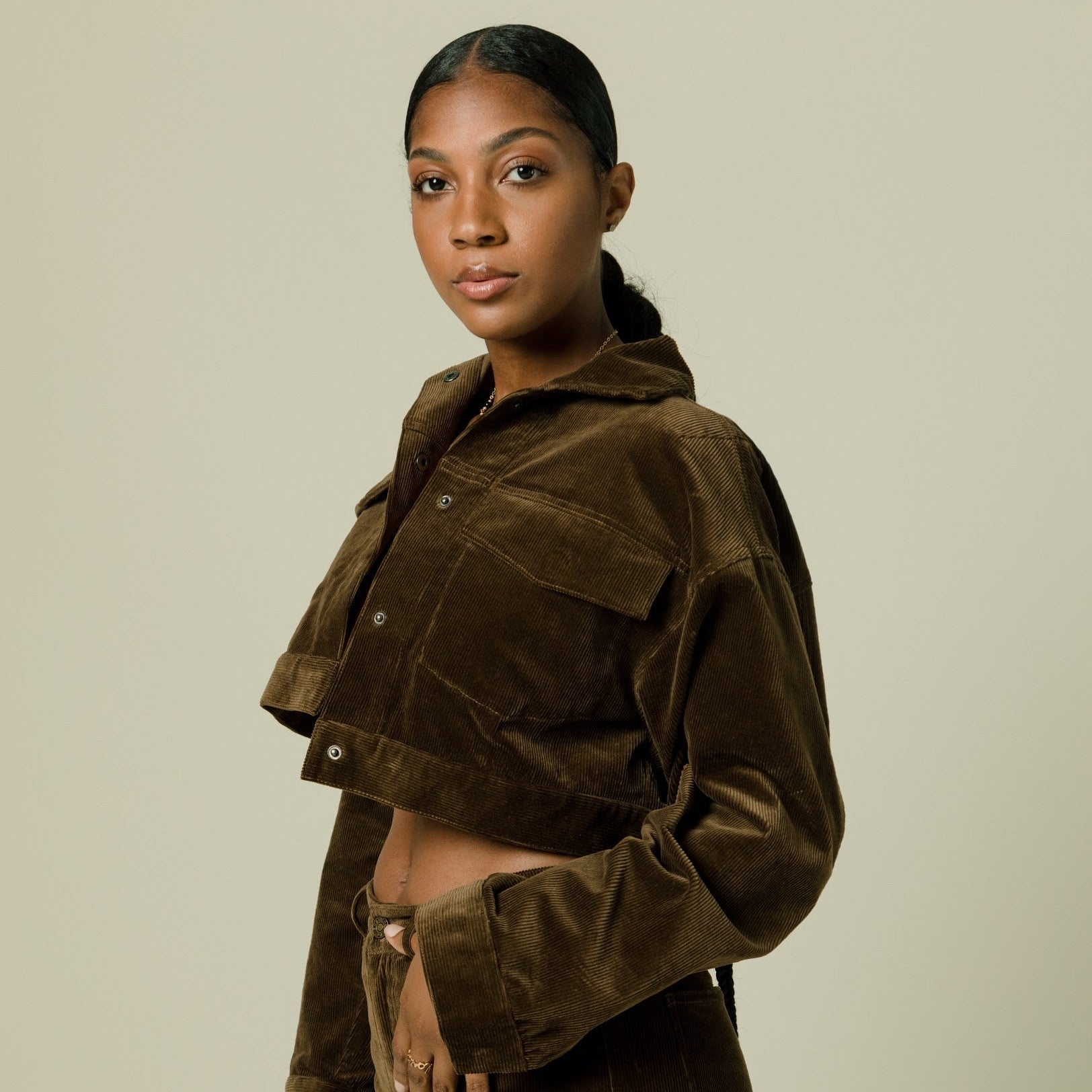 Woman wearing a brown corduroy jacket and pants against a beige background